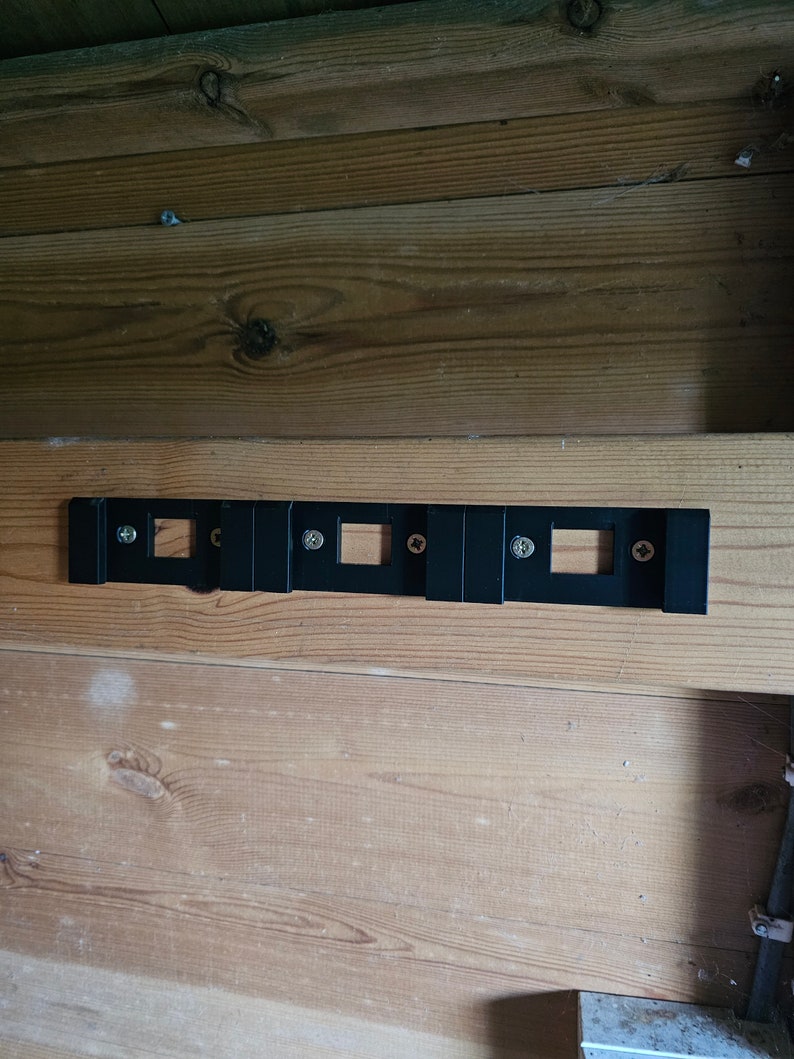 May include: A black metal wall mount with five rectangular openings and four screws. The mount is attached to a wooden wall.