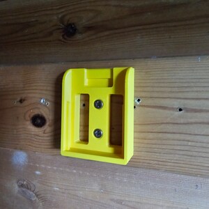 May include: A yellow plastic wall mount with two screws. The mount has a rectangular shape with a slot in the center.