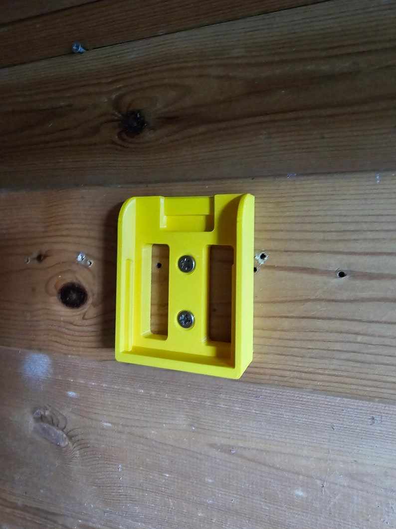 May include: A yellow plastic wall mount with two screws. The mount has a rectangular shape with a slot in the center.