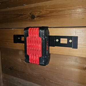 May include: A black and red power tool battery with the text "Pro CORE 18V" on the side, mounted on a wooden wall with a black metal bracket.