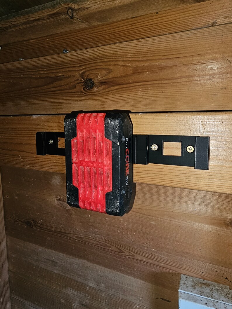 May include: A black and red power tool battery with the text "Pro CORE 18V" on the side, mounted on a wooden wall with a black metal bracket.