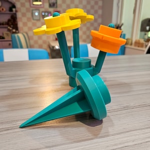 May include: A teal plastic garden stake with three yellow and orange flower-shaped toppers. The stake has a pointed end for inserting into the ground.
