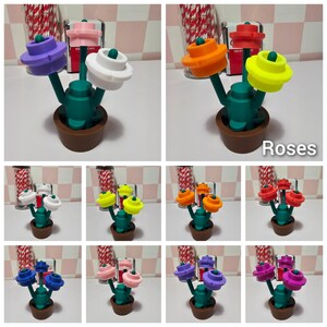 Puede incluir: Un juego de tres saleros y pimenteros con forma de flor en una variedad de colores, incluyendo morado, blanco, naranja, amarillo, rojo y rosa. Los saleros est&aacute;n dispuestos en una peque&ntilde;a maceta con un tallo verde y una base marr&oacute;n. El texto "Roses" est&aacute; impreso debajo de la imagen.