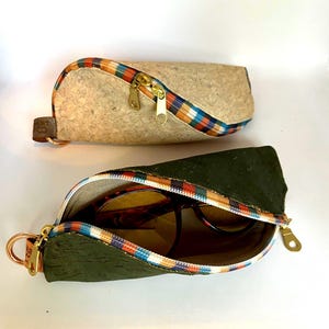以下が含まれることがあります： ジッパー付きのコルク製メガネケース2個。1つはベージュでカラフルな格子柄のジッパー引き手、もう1つはグリーンでカラフルな格子柄のジッパー引き手。グリーンのケースにはサングラスが入っています。