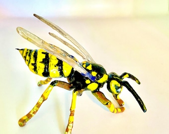 Könnte beinhalten: Eine gelbe und schwarze Wespenfigur mit durchsichtigen Flügeln. Die Wespe ist in Flugposition mit ausgestreckten Beinen dargestellt.