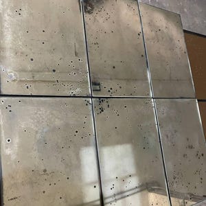 May include: A set of six rectangular glass mirror panels arranged in a grid. Each panel features an aged, distressed finish with dark, mottled spots and oxidation marks across the reflective surface, creating a weathered and antique appearance.