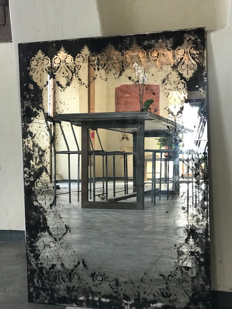 May include: A large, antique-style mirror with a black frame and a distressed, white-painted design. The mirror reflects a room with a wooden table and chairs.