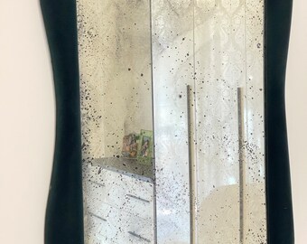 May include: A dark green, irregularly shaped mirror with a distressed, antique-style glass. The mirror is framed in a thick, velvet-like material.