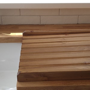 Puede incluir: Tabla de pan rectangular de madera clara con ranuras para recoger las migas. La tabla est&aacute; sobre una encimera de madera junto a un fregadero blanco. La tabla mide aproximadamente 38 cm por 30 cm.