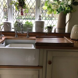 Puede incluir: Una cocina de estilo r&uacute;stico con un fregadero de porcelana blanca y un grifo cromado. Una tabla de cortar de madera y un hervidor el&eacute;ctrico blanco se encuentran sobre la encimera de madera. Plantas y flores verdes adornan la ventana.