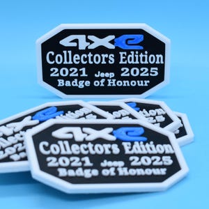 May include: A collection of black and white badges with the text "4xe Collectors Edition 2021 Jeep 2025 Badge of Honour" in white and blue. The badges have a unique hexagonal shape and are arranged on a light blue background.