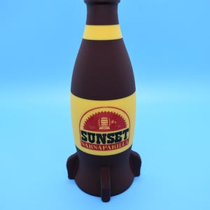 May include: A brown glass bottle with a red cap and yellow stripes. The bottle is shaped like a rocket and has a label that says "Sunset Sarsaparilla".