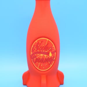 May include: A red rocket-shaped bottle with a yellow and red label that says "Nuka Orange".