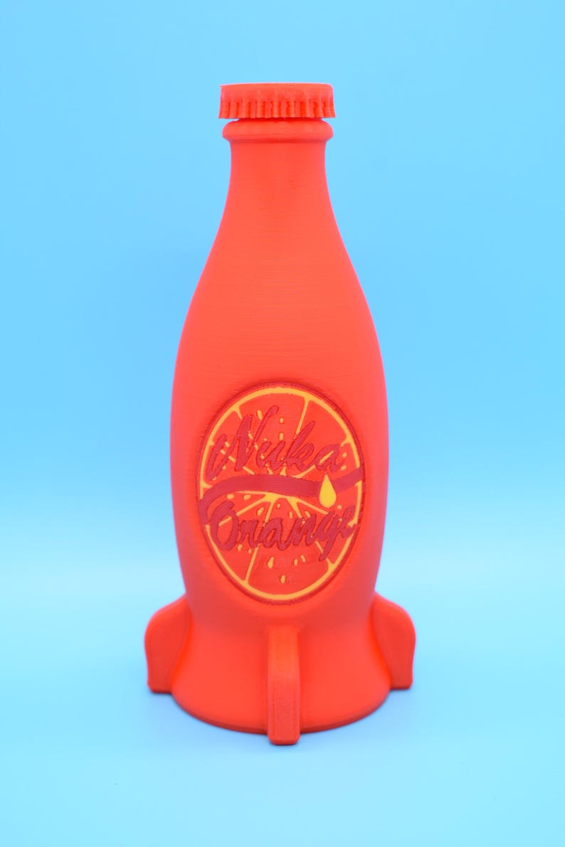 May include: A red rocket-shaped bottle with a yellow and red label that says "Nuka Orange".