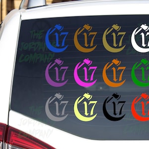 May include: A collection of vinyl car decals featuring the number 17 with an axe design. The decals are available in various colors, including blue, orange, green, and black. The text "THE JORDAN COMPANY" is visible on the car window.