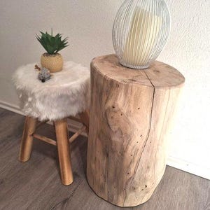 Könnte beinhalten: Ein weißer Kunstfellhocker mit Holzbeinen und ein Beistelltisch aus natürlichem Baumstammholz mit einem weißen Draht-Kerzenhalter darauf.