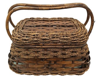 May include: A rectangular brown woven basket with a lid and a handle. The basket is made of natural materials, with a woven pattern on the sides and lid. The handle is made of curved bamboo. The basket is suitable for storage or display.