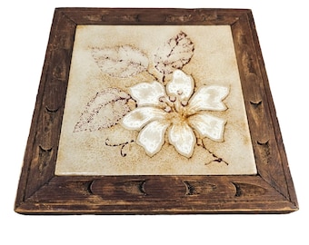 May include: A brown wooden framed tile with a white flower and brown leaves on a beige background.