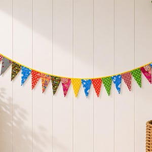 May include: A vibrant fabric bunting featuring triangular flags in a variety of patterns and colours, such as red polka dots, green, blue, and floral designs. The flags are strung on a yellow cord, creating a cheerful decoration.