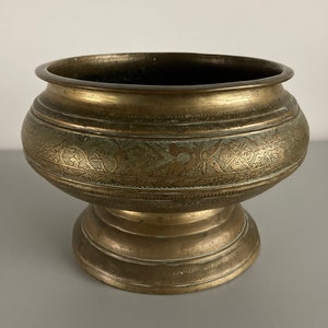 May include: A vintage brass bowl with intricate engraved floral designs. The bowl has a wide, rounded base and a flared lip. It is a beautiful example of traditional craftsmanship.