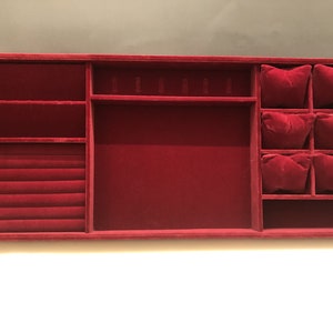 May include: A red velvet jewelry organizer with compartments for rings, earrings, and necklaces. The organizer has a large central compartment and a section with six small compartments.