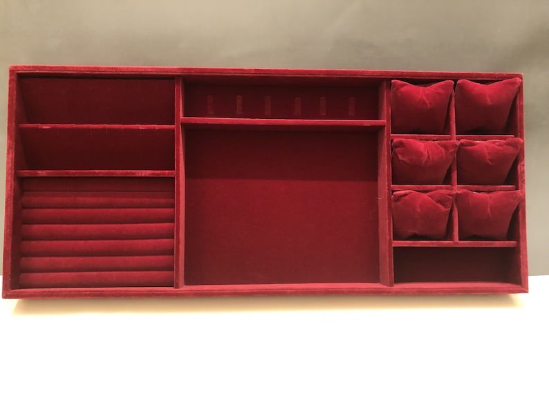 May include: A red velvet jewelry organizer with compartments for rings, earrings, and necklaces. The organizer has a large central compartment and a section with six small compartments.