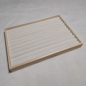 May include: A wooden ring display tray with a light brown finish and a white velvet lining. The tray has multiple slots for storing rings.