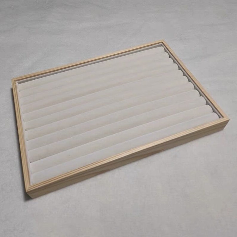 May include: A wooden ring display tray with a light brown finish and a white velvet lining. The tray has multiple slots for storing rings.