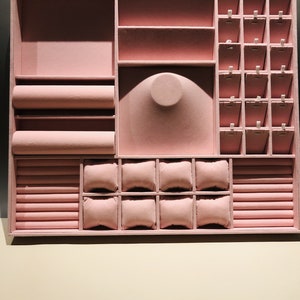 May include: A pink velvet jewelry box with compartments for rings, earrings, necklaces, and bracelets. The box has a ring roll, a watch cushion, and a necklace holder.