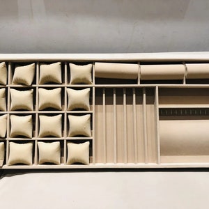 May include: A wooden jewelry box with a beige velvet interior. The box has multiple compartments for storing rings, earrings, necklaces, and other jewelry. The compartments are lined with beige velvet.