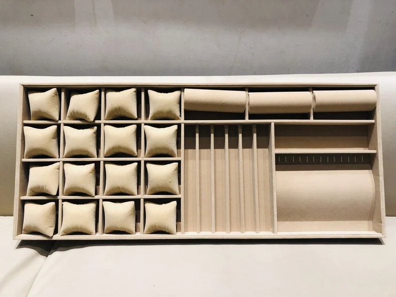 May include: A wooden jewelry box with a beige velvet interior. The box has multiple compartments for storing rings, earrings, necklaces, and other jewelry. The compartments are lined with beige velvet.
