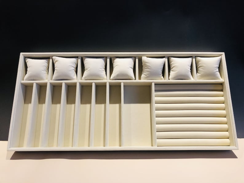 May include: A white jewelry tray with compartments for rings, bracelets, and watches. The tray has a velvet lining and a ring roll.