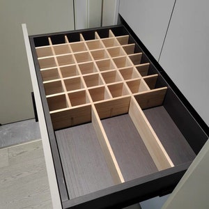 Puede incluir: Un organizador de cajones de madera con múltiples compartimentos. El organizador está hecho de madera marrón claro y tiene un marco marrón oscuro.