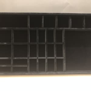 May include: Black velvet jewelry organizer with multiple compartments of varying sizes. The organizer is rectangular and has a smooth surface.