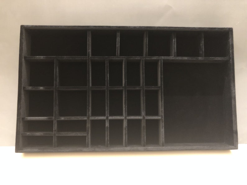 May include: Black velvet jewelry organizer with multiple compartments of varying sizes. The organizer is rectangular and has a smooth surface.