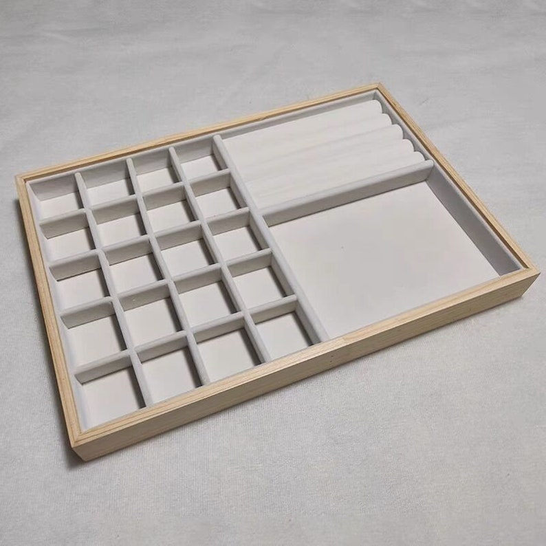 May include: A wooden jewelry box with a white velvet interior. The box has 24 small compartments and a larger section for rings.