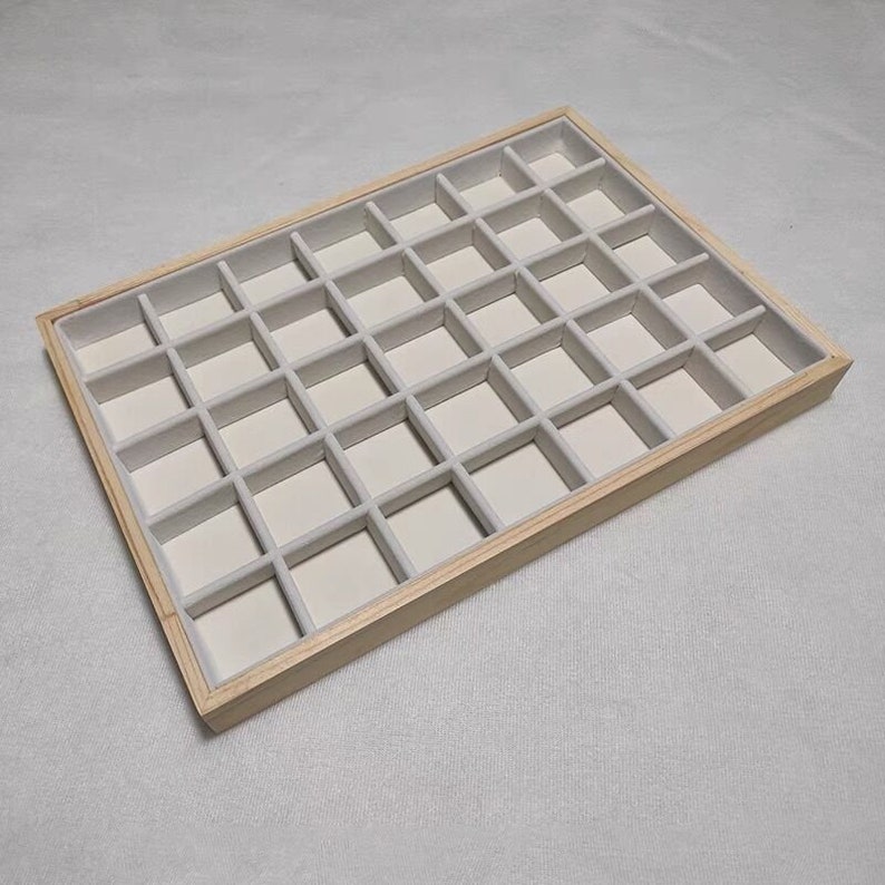May include: A wooden jewelry storage tray with 36 compartments lined with light gray felt.