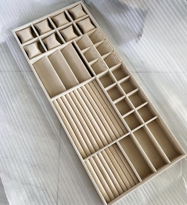 May include: A beige velvet jewelry organizer with compartments for rings, bracelets, necklaces, and watches. The organizer has a variety of compartments, including a ring roll, a watch pillow, and a necklace holder.