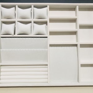 May include: White jewelry organizer with multiple compartments for storing rings, bracelets, watches, and earrings. The organizer has a velvet lining and is made of wood.