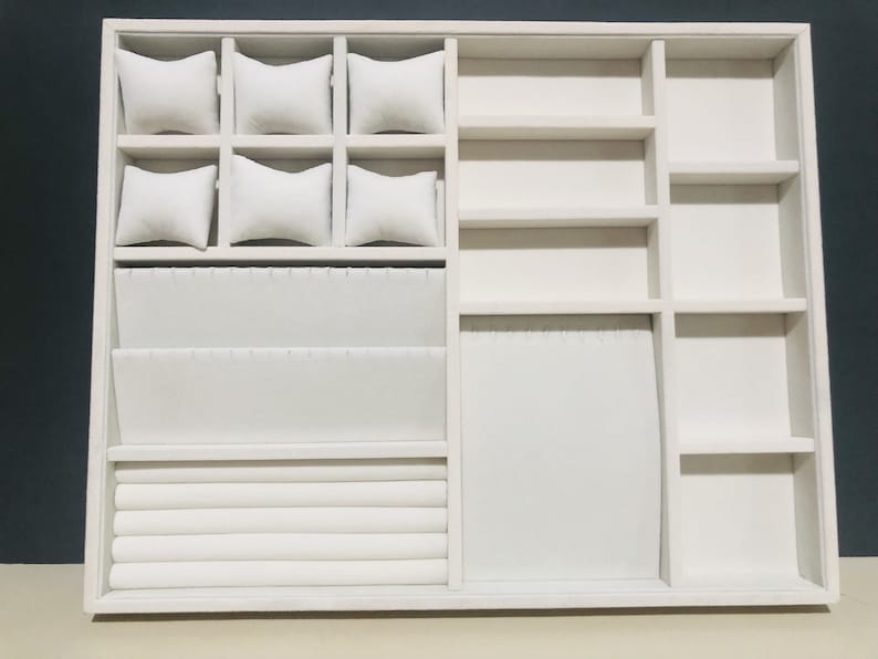 May include: White jewelry organizer with multiple compartments for storing rings, bracelets, watches, and earrings. The organizer has a velvet lining and is made of wood.