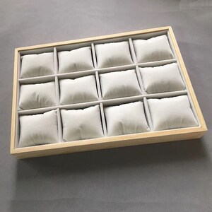 May include: A wooden watch box with twelve individual compartments lined with soft, white fabric cushions.
