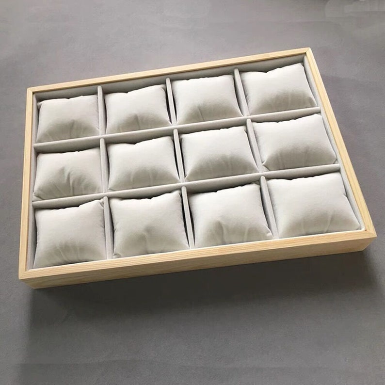 May include: A wooden watch box with twelve individual compartments lined with soft, white fabric cushions.