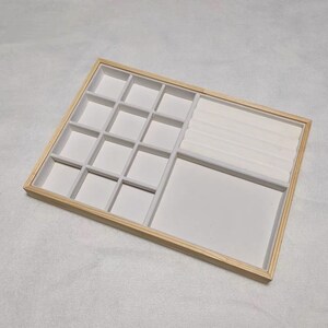 May include: A wooden jewelry box with a white velvet interior. The box has 15 compartments for storing small items, and a long slot for rings or bracelets.