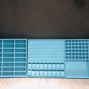 May include: Three light blue velvet-lined jewelry storage boxes with different compartments. The box on the left has a grid of small squares, the middle box has a row of larger squares, and the box on the right has a grid of smaller squares and a long, narrow compartment.