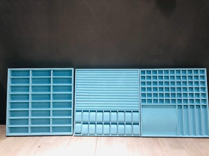 May include: Three light blue velvet-lined jewelry storage boxes with different compartments. The box on the left has a grid of small squares, the middle box has a row of larger squares, and the box on the right has a grid of smaller squares and a long, narrow compartment.