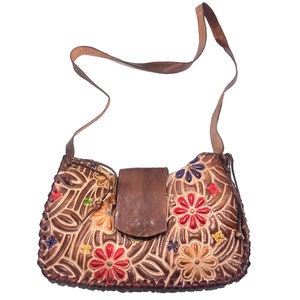 May include: A brown leather shoulder bag with a flap closure and floral embroidery in shades of red, yellow, blue, and green.