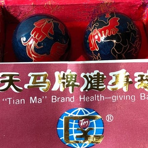 May include: Two blue and gold Chinese exercise balls with red and gold painted dragons. The balls are in a red velvet box with a label that reads "Tian Ma" Brand Health-giving Balls. The label also has a gold globe with a "TM" inside.