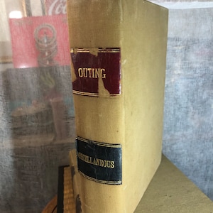 May include: A tan-coloured book with the word "OUTING" in gold lettering on a red background. The book has a black label with the word "MISCELLANEOUS" in gold lettering.