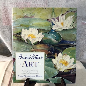 May include: A book titled "Beatrix Potter's Art" with a watercolor painting of white water lilies on the cover. The book is about paintings and drawings selected and introduced by Anne Stevenson Hobbs.