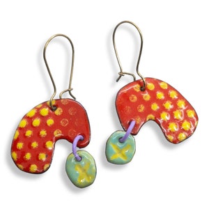 May include: A pair of handmade earrings featuring red and yellow enamel with green and yellow accents. The earrings are shaped like a crescent moon and have a dangling charm.